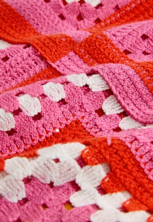 Manta de ganchillo con hilos vibrantes de color rosa, rojo y blanco. Presenta patrones intrincados, puntos texturizados y un diseño en capas.