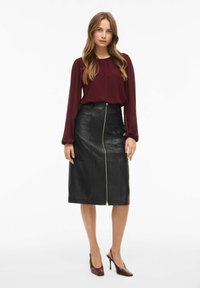 Gonna midi in pelle nera con zip frontale, abbinata a una blusa bordeaux a maniche lunghe. La gonna presenta una vestibilità sartoriale e una texture liscia.