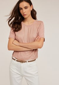 Top scurt de culoare roz deschis, cu mâneci scurte, având un design cu paiete pe față, gât rotund, asortat cu pantaloni albi și o curea de piele maro cu un fermoar decorativ.