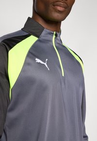 Felpa atletica grigia con accenti neri e pannelli verdi brillanti. Presenta un design a metà zip e un logo Puma bianco sul petto.