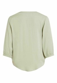 Ljusgrön blus med trekvartsärmar, rundad nederkant och mjuk, slät textur. Har samlad detalj vid ärmarnas manschetter.