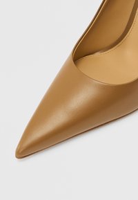 Spids tå højhælet sko i lyst brunt læder med en glat tekstur og et udskåret side-design, der fremviser en indvendig beige foring.