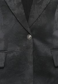 Black textured blazer featuring a subtle patterned design, a single button closure, and two front pockets, made from a smooth fabric.