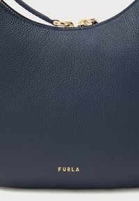 Navy ādas rokassoma ar teksturētu virsmu, ar zelta rāvējslēdzēju un zelta "FURLA" logotipu apakšā.