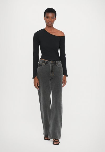 Top nero a spalla unica in tessuto knit aderente abbinato a jeans in denim scuri a vita alta e con vestibilità ampia. La modella indossa sandali neri con strap.
