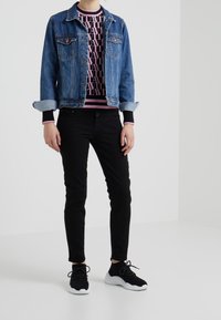 Chaqueta de mezclilla en azul medio con mangas remangadas, suéter negro y rosa con un diseño debajo, pantalones negros ajustados y zapatillas negras con suelas blancas.