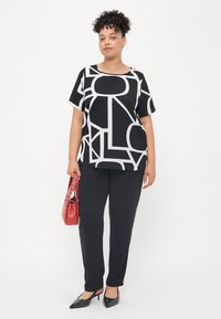 Black and white patterned top with geometric designs, paired with black pants, red handbag, and black pointed shoes with studs.