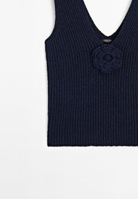 Námořnický pletený top s ribovanou texturou. Má hluboký V-výstřih a detail háčkované květiny na levé straně. Jednoduchý a přiléhavý design.