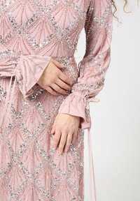 Rosa Kleid mit paillettenverzierten geometrischen Mustern, mit Rüschensäumen und einer taillierten Taille mit einer Schleife.