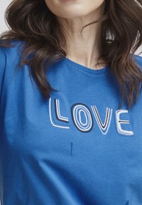 Camiseta de algodón azul con bordado de "LOVE" en diferentes tonos de azul y negro, con un cuello redondo y una textura suave.