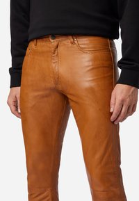 Bruine leren broeken met een gladde textuur, voorzien van een klassieke vijf-pocketontwerp en een knoopsluiting, gedragen met een zwarte trui.