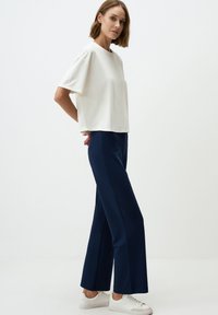 Witte top met korte mouwen, gecombineerd met marineblauwe wijde broek en witte sneakers. Glad materiaal met een relaxte pasvorm en strakke lijnen.