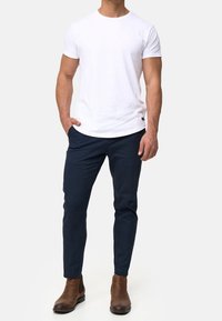 Biała bawełniana koszulka z okrągłym dekoltem, zestawiona z ciemnogranatowymi spodniami i brązowymi skórzanymi botkami za kostkę. Prosty, dopasowany krój.