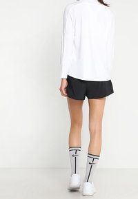 Camiseta blanca de manga larga, pantalones cortos negros, calcetas gris de altura de rodilla con detalles en negro y zapatillas deportivas blancas. Diseño y esquema de color simple.