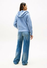 Hellblauer Kapuzenpullover mit lockerer Passform, kombiniert mit weit geschnittenen, verblassten blauen Jeans. Weiche Texturen und lässiges Design.