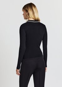 Maglia nera a maniche lunghe con trama a coste e silhouette aderente. Presenta un colletto rotondo con dettagli bianchi sul retro. Texture liscia, design minimalista.