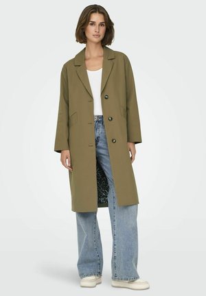 Cappotto lungo verde oliva con colletto a punte, due tasche frontali e interno con stampa leopardata nera. Abbinato a jeans a gamba larga blu chiaro.