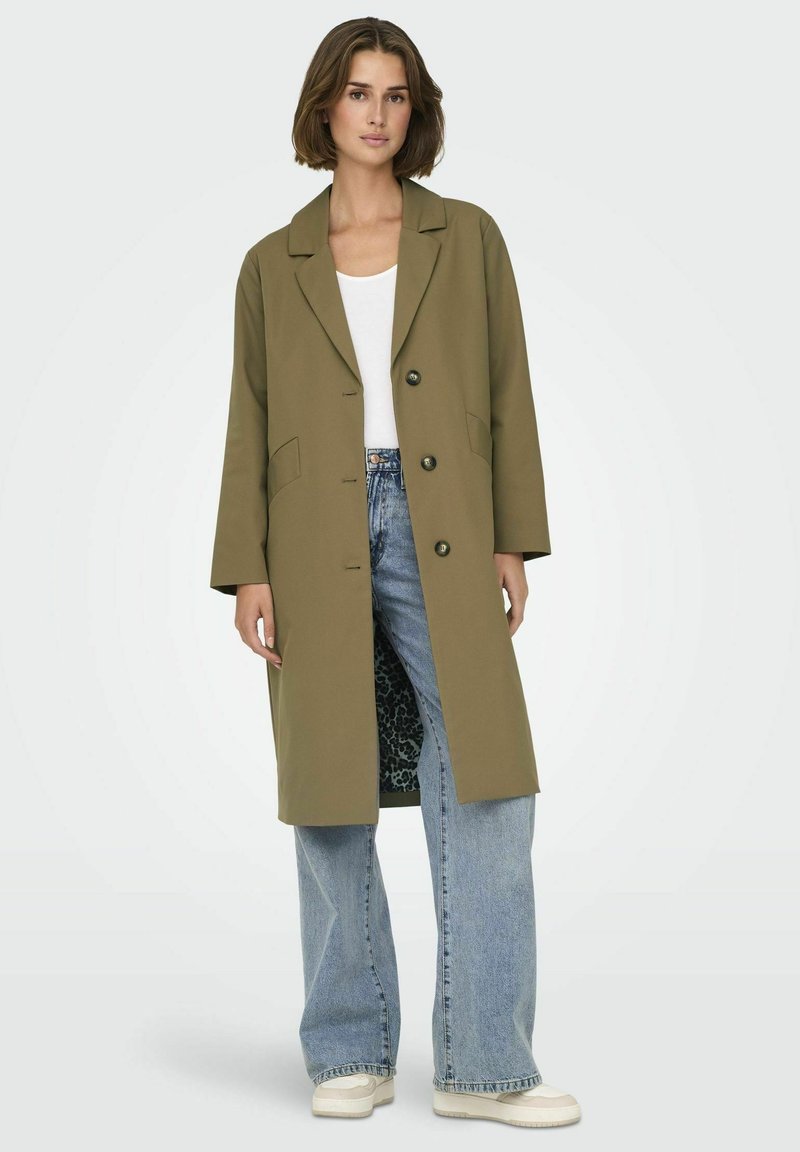 Cappotto lungo verde oliva con colletto a punte, due tasche frontali e interno con stampa leopardata nera. Abbinato a jeans a gamba larga blu chiaro.