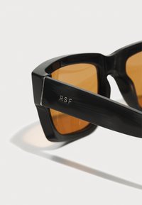 Mustad mustad prillid nurgeliste raamidega, millel on merevaiguvärvi läätsed ja hõbedane aktsent, millel on küljel graveeritud "RSF".