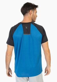 Camiseta deportiva de manga corta en azul y negro, con un patrón texturizado, un detalle reflectante en la parte posterior y un logo cerca del escote.