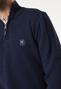 Navyblauer Reißverschluss-Pullover aus strukturiertem Strickstoff, mit geripptem Kragen und Logopatch auf der Brust, der über ein tailliertes Design verfügt.