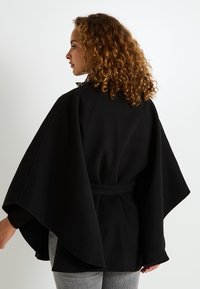 Abrigo estilo capa negro con mangas anchas, hecho de una tela suave, que cuenta con una cintura ceñida y un cuello de leopardo en contraste.