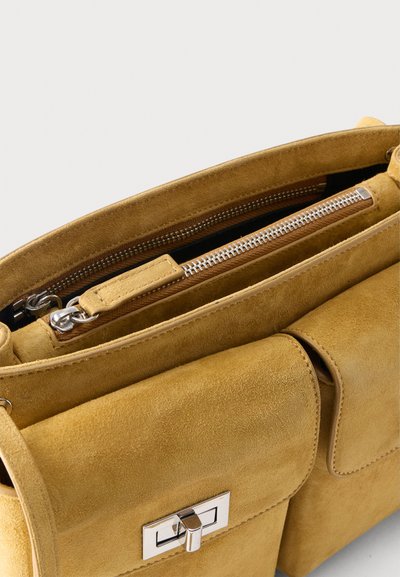 Τσάντα χειρός από σουέντ σε ταμπά χρώμα με δύο μπροστινές θήκες, ασημένιες κλειδαριές με στροφή και επάνω χώρο με φερμουάρ, εμφανιζόμενη μερικώς ανοιχτή.