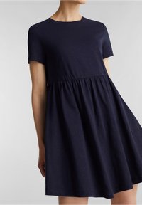 Lyhyet hihalat navy blue -mekko pehmeästä kankaasta, jossa on rypistetty vyötärö ja levenevä hame, esittäen sileää tekstuuria ja klassista siluettia.