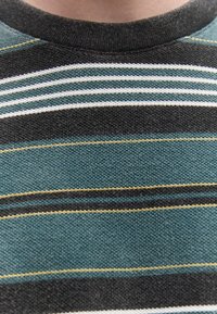 Κοντινό πλάνο μαύρου και τιρκουάζ ριγωτού πλεκτού πουλόβερ με λευκές και κίτρινες διακοσμητικές γραμμές γύρω από το λαιμό.