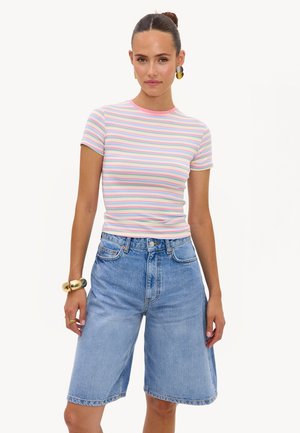 Femme portant un haut à manches courtes rayé pastel, un short en jean bleu clair jusqu'aux genoux, des boucles d'oreilles en or et un bracelet en or.