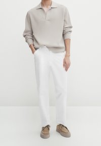 Pull en tricot côtelé beige avec un col, associé à un pantalon droit blanc et des chaussures marron clair. Design minimaliste, texture lisse.