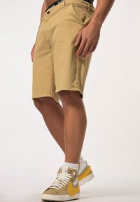 Khaki shorts met een slim fit, een knoopsluiting en voorvakjes. Gecombineerd met witte sokken en beige sneakers met gele accenten.