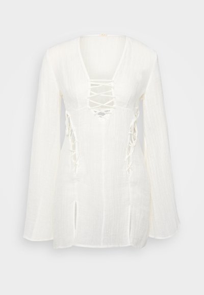 Haut blanc à manches longues avec un décolleté en V et un devant à lacets. Présente des découpes latérales et un tissu texturé. Coupe décontractée avec des manches évasées.