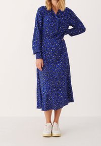 Pitkät hihat, sininen mekko, jossa on lepakkokuvio, napitettu etuosa ja väljä malli, yhdistettynä valkoisiin lenkkareihin.