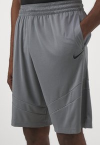 Pantalones cortos deportivos grises hechos de una tela de malla transpirable que cuentan con una cinturilla elástica, bolsillos laterales y un acento de logo negro.