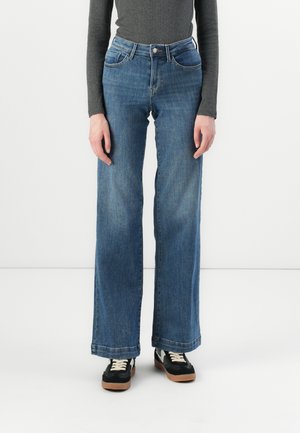 Breda byxor i blå denim med en urtvättad finish, med en klassisk femfickorsdesign och knappstängning. Tyget är denim med en mjuk textur.