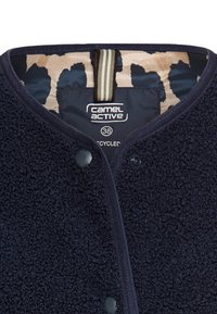 Marineblauwe fleecvest met een gestructureerd oppervlak, voorzien van drukknoopsluitingen en een beige en marineblauw gestreepte voering. Tekst luidt "camel active 38 gerecycled."
