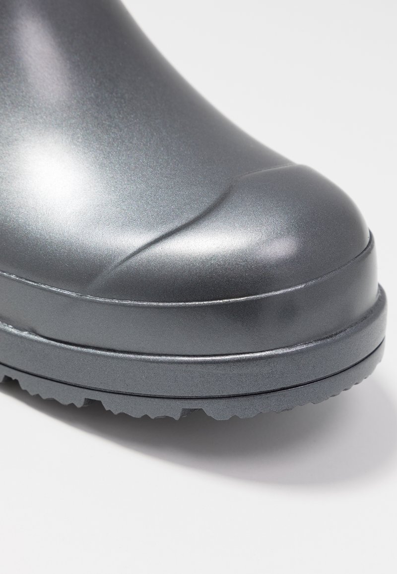 Botas de goma grises con acabado brillante, punta redondeada, suela texturizada y ligeros detalles de diseño en el borde superior.