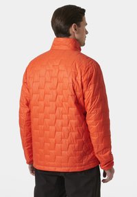 Chaqueta acolchada naranja con un patrón de cuadro, cuello alto y mangas largas. La tela tiene un acabado suave y brillante.