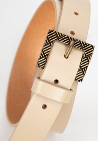 Cinturón de cuero beige con una hebilla metálica con diseño y acabado en bronce. El cinturón cuenta con agujeros para ajustar el tamaño y tiene una textura suave.