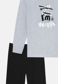 Gray long-sleeve top with a graphic print in black and white reading "I'm UN'IQUE" paired with black pants, made from soft, lightweight fabric.