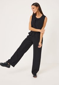 Top senza maniche nero con scollatura rotonda e dettagli arricciati, abbinato a pantaloni neri larghi con vita elastica e cordino.