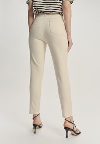 Beżowe spodnie o slim fit, wysokim stanie i dwóch tylne kieszeniach. Połączone z czarnymi sandałami na obcasie i paskowanym topem. Gładki, teksturowany materiał.