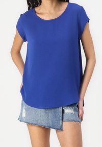 Blue short-sleeve top in a smooth fabric, featuring a round neckline and relaxed fit. Paired with a distressed denim mini skirt.