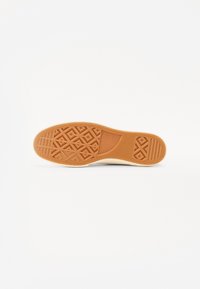 Talpă de cauciuc cu un grip texturat în formă de diamant. Culoare bej deschis cu o margine internă albă și branding "Converse".