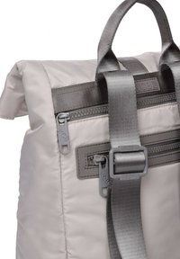 Mochila de nailon gris claro con tapa plegable, que cuenta con cierres de cremallera grises, correas resistentes y un detalle central de hebilla.