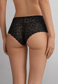 Schwarze Spitzenunterwäsche mit kunstvollen floralen Mustern, gewellten Kanten und einer halbtransparenten Textur. Das Design hat einen Hipster-Schnitt.