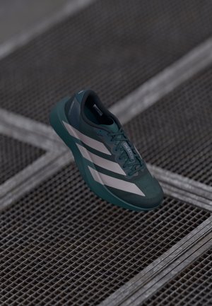 Dark teal athletic shoe with a textured upper, featuring three white stripes, a rounded toe, and a cushioned sole.