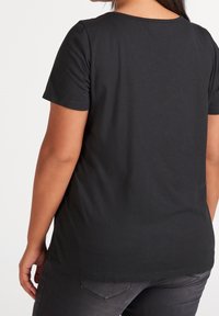 Person wearing a plain black short-sleeve t-shirt and dark gray jeans, shown from the back against a white background.