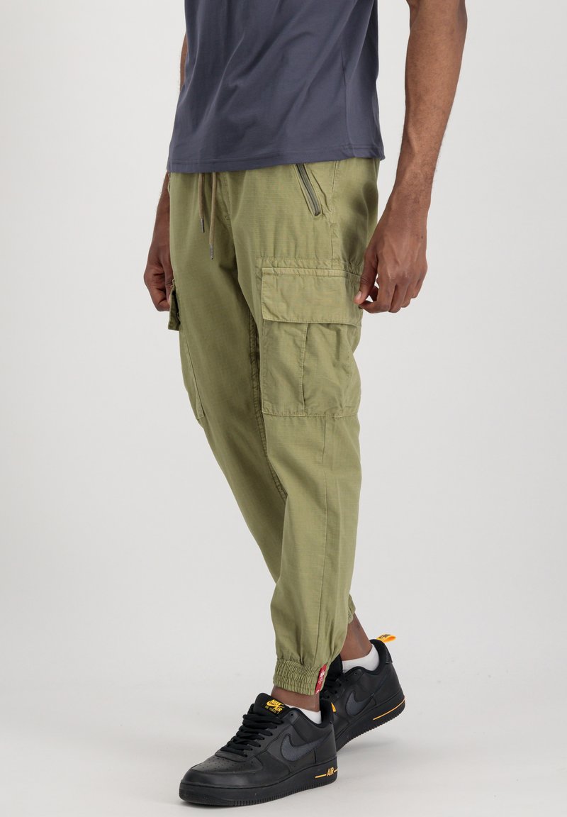 Khaaki spodnie cargo mają wiele kieszeni, elastyczne mankiety i pasek ze sznurkiem; zestawione z czarnymi sneakersami i szarym t-shirtem.